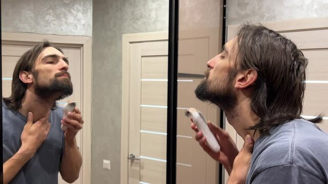 Young man trimming his neckline with a trimmer while looking in the bathroom mirror, focusing on grooming and style