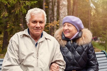 Fototapeta premium Happy senior man and old woman sitting on the bench in autumn park. Elderly couple outdoor portrait