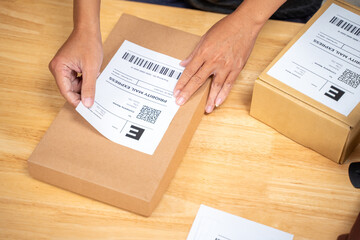 Close up hands of an online seller man putting shipping label on the product box before sending it off to his customer