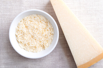 Grated parmesan cheese, Parmigiano Reggiano in a wooden bowl on linen, with whole piece of cheese on the right side. Italian hard, granular cheese, produced from cow's milk, aged at least 12 months.