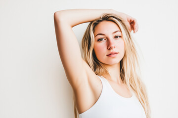 Obraz premium A close-up portrait of a young blonde woman wearing a white tank top, posing against a white background. Relaxed, confident expression with her arm raised, natural beauty of sport life.