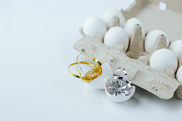 There are eggs in an egg tray and a shell with tinsel next to it on a white background