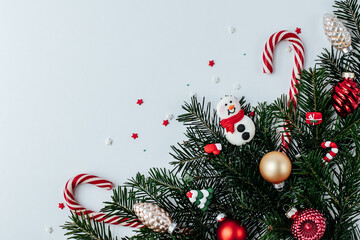 in the lower right corner there is a spruce branch with New Year's decor of a snowman, Christmas balls and candies on a white background