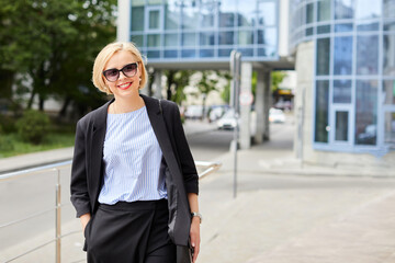 Fototapeta premium Beautiful blonde young woman wearing suit and walking on the street. A woman dressed in a business style walks around the city