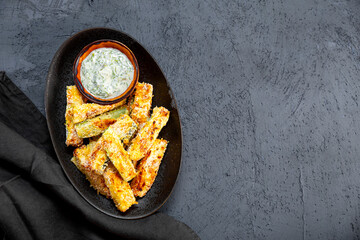 Healthy zucchini fries with yogurt and herbs sauce on dark background with copy space