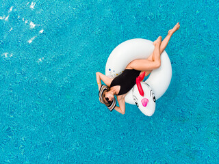 Beautiful woman in swimsuit on inflatable unicorn pool float in pool in the hotel drone aerial view. Summer holidays