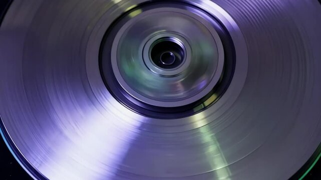 Close up of a metallic disk with a circular pattern reflecting purple and green light, conveying a sense of technology and motion