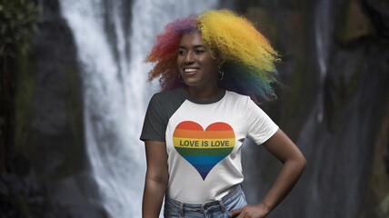 A girl with rainbow Afro curls stands at a waterfall, bright emotional smile, photo. In a T-shirt: love is love. Generative AI