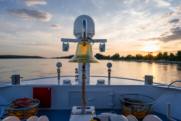 cruise ship at sunset, chrome railing on sun deck, on river with water, forest, bank in danube...