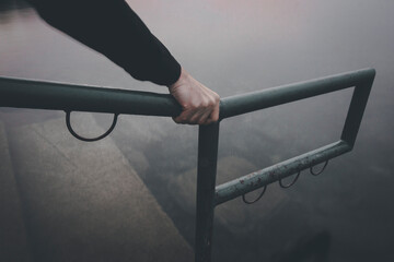 Close up photograph of a lone hand tightly gripping an old metal railing with peeling paint.