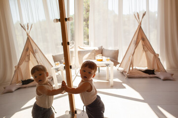 Small child under one year old plays in the room against the backdrop of wigwam in beige shades. The infant baby is happy and dressed  bodysuit. The cozy home environment © Вероника Зеленина