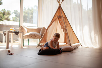 Small child under one year old plays with cat in the room against the backdrop of wigwam in beige shades. The infant baby is happy and dressed  bodysuit. The cozy home environment © Вероника Зеленина
