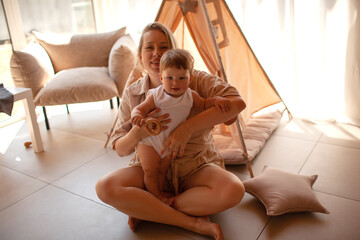 Small child under one year old plays in the room against the backdrop of wigwam in beige shades. The infant baby is happy and dressed  bodysuit. The cozy home environment © Вероника Зеленина