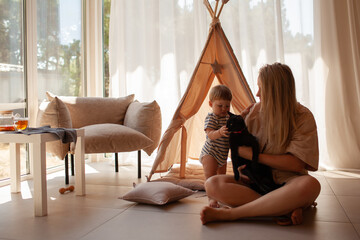 Small child under one year old plays in the room with mom against the backdrop of wigwam in beige shades. The infant baby is happy and dressed  bodysuit. The cozy home environment © Вероника Зеленина