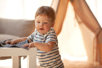 Small child under one year old plays in the room against the backdrop of wigwam in beige shades. The infant baby is happy and dressed  bodysuit. The cozy home environment © Вероника Зеленина