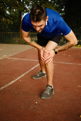 Knee Pain. Sports injury. Young man has knee pain during outdoor exercise. Sports running knee injury in male runner on the treadmill near the stadium.