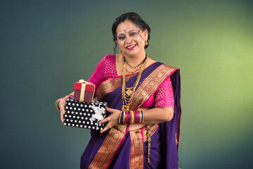 Happy traditional Indian woman wearing saree holding and posing with gift box