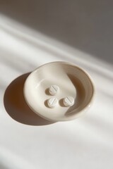 Three white tablets in a minimalist ceramic bowl on a light background.