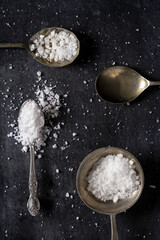 Top view of a spoons with coarse grained sea salt on black background. Flat lay. Top view. Food concept.