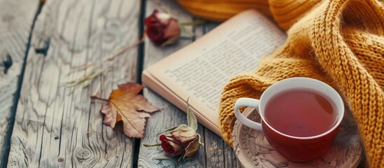 Fall background Autumn arrangement featuring hot tea a book a dry rose flower and a knitted sweater A cup of hot tea and a knitted scarf on a wooden table Autumn reading list Weekend relaxation durin