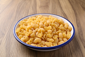 Raw macaroni pasta in bowl on wooden background, Food ingredient