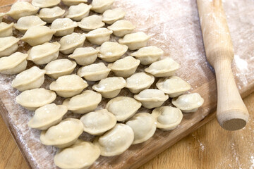 Raw dumplings were laid out on a wooden board for cooking. Next to it is a rolling pin for rolling out the dough. The filling is minced meat, potatoes, cheese or cottage cheese.