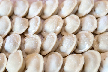 The raw dumplings were placed on a wooden cooking board, sprinkled with flour. The filling is minced meat, potatoes, cheese or cottage cheese. A semi-finished product, ready for cooking.