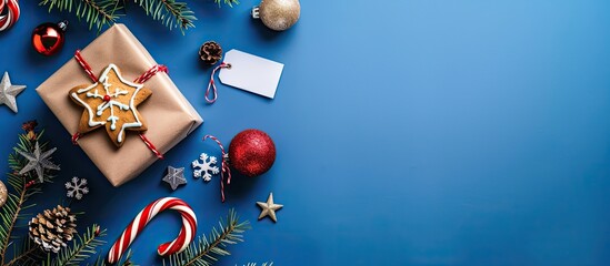 Festive frame featuring a gift box pine branch blank shopping tag stars candy cane gingerbread cookie and festive balls on a blue background horizontal orientation copy space top view