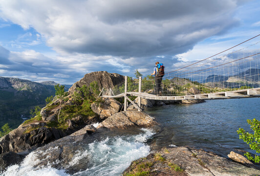 Hiker walking over the small footbridge over the Litlverivass forsen waterfall in National Park Rago, Norway.
