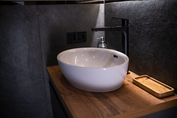 Modern white ceramic sink on wooden countertop in contemporary bathroom with stylish fixtures and ambient lighting