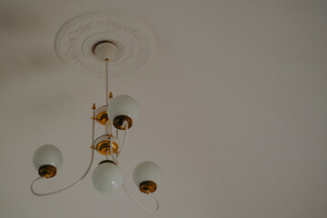 A vintage-style chandelier with glass globes hanging from a decorative ceiling rose in a softly lit...