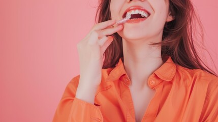 A woman in an orange shirt enjoys a sweet treat, her smiling mouth amplifying the joy against a vibrant pink background.
