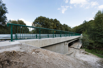 
A new modern automobile bridge over the river on the background of the blue sky. A sturdy reinforced concrete bridge, thick concrete pillars and metal floors.