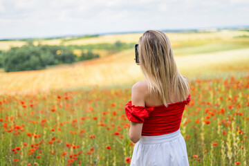 Blonde young woman takes a photo with a phone in a field of red poppies