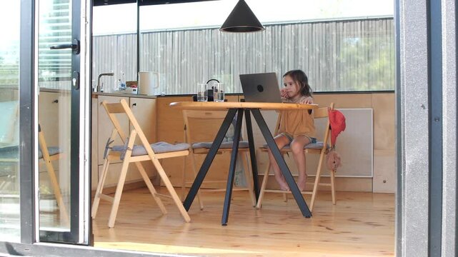 Young girl sitting at a table using a laptop in a tiny house