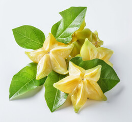 Fototapeta premium Several star fruits with leaves and stems on a white backdrop, one cut to reveal a bright and translucent surface.