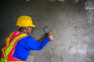 A male construction worker using a trowel to plaster the wall of a house inside a room of a new house under construction, Asian worker male plastering cement on a wall of the house