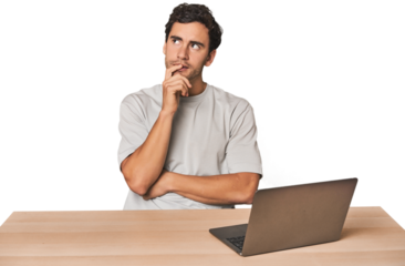 Hispanic young man working on laptop looking sideways with doubtful and skeptical expression.