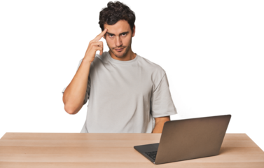 Hispanic young man working on laptop pointing temple with finger, thinking, focused on a task.