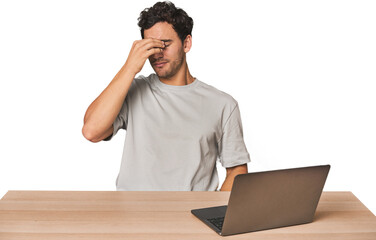 Hispanic young man working on laptop having a head ache, touching front of the face.