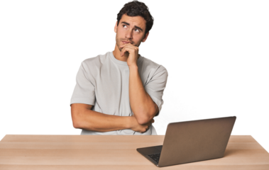 Hispanic young man working on laptop thinking and looking up, being reflective, contemplating, having a fantasy.