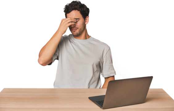 Hispanic young man working on laptop having a head ache, touching front of the face.