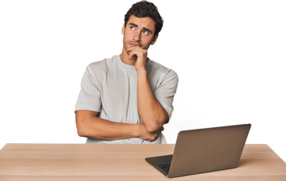 Hispanic young man working on laptop thinking and looking up, being reflective, contemplating, having a fantasy.