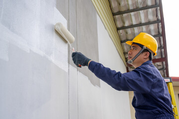A painter of a newly built house, A painter holding a paint roller skillfully paints a house. A...