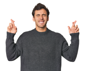 Young Hispanic man in studio crossing fingers for having luck