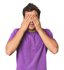 Young Hispanic man in studio afraid covering eyes with hands.