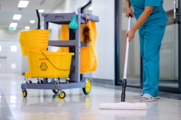 A close-up of mop mopping floor cleaning in office with cleaning cart and floor cleaning tools and...