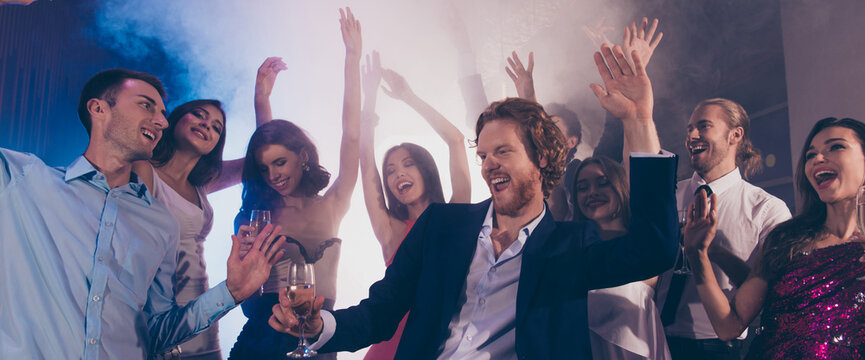 Good-looking man in formalwear dress-code vip dance with glass of beverage against group of fancy luxury friends raised hands up make toothy smile