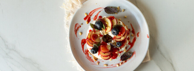 bagel with cream cheese, peaches and blueberries on a white plate on a light table, top view