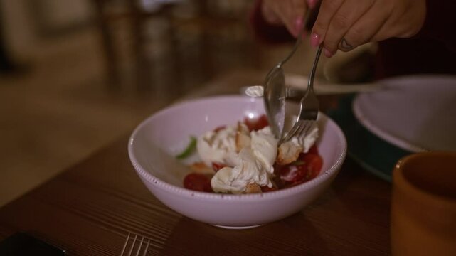 Woman with pink nails eating a delicious tomato, cheese, and bread salad using a fork and spoon in an italian restaurant, indoors, capturing the essence of casual dining with fresh ingredients.